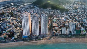 An aerial view of a coastal city with high-rise buildings, a beach, and mountains in the background.