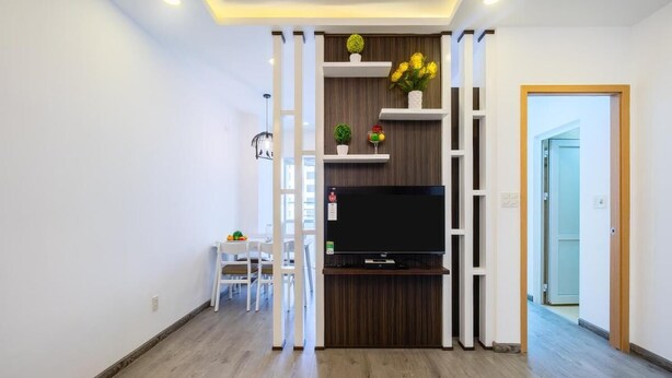 A modern living room with a flat-screen TV, white furniture, and decorative plants.