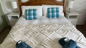 A bed with a checkered pillow, a white quilt, and a wooden headboard. - The Stables - Crackington Haven Cornwall (Crackington Haven)