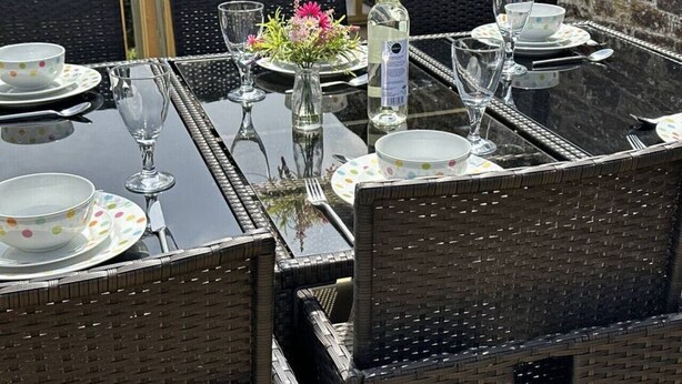 A dining table set with plates, glasses, and cutlery, surrounded by wicker chairs. - The Stables - Crackington Haven Cornwall (Crackington Haven)