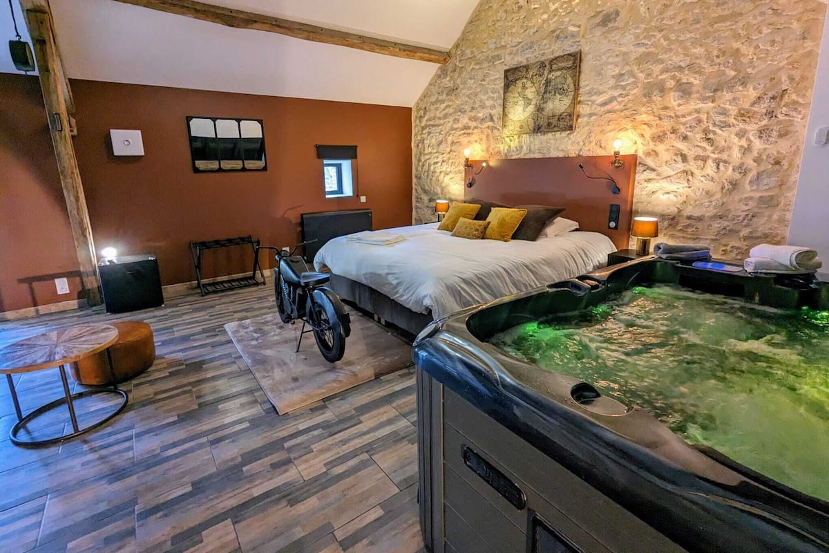 Quarto com parede de pedra, cama, banheira de hidromassagem e uma motocicleta.