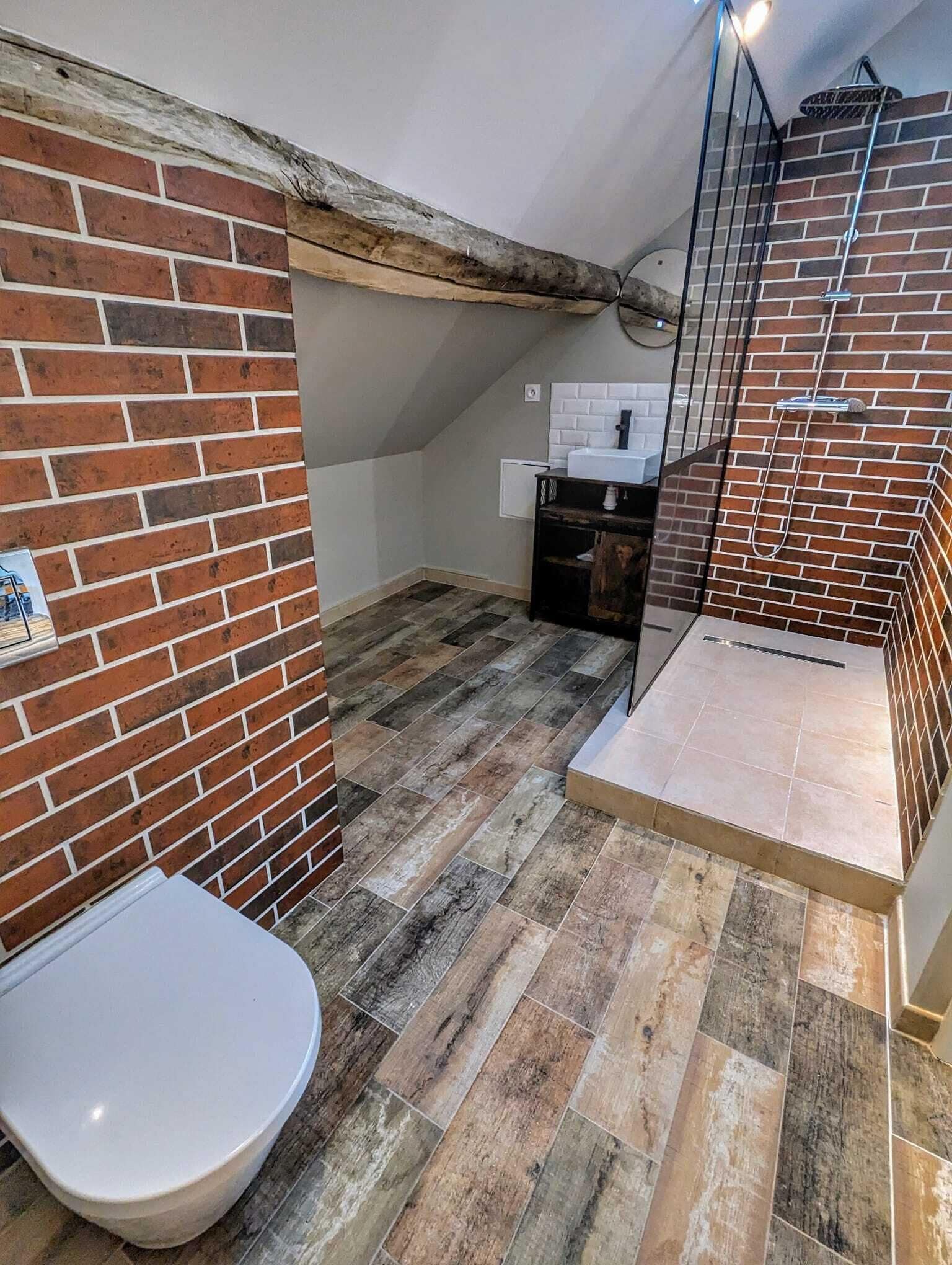 Een kleine badkamer met toilet, douchecabine met glazen deur en betegelde vloer.