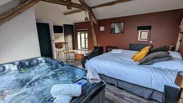 A room with a large bed, a hot tub, and a wooden ceiling.