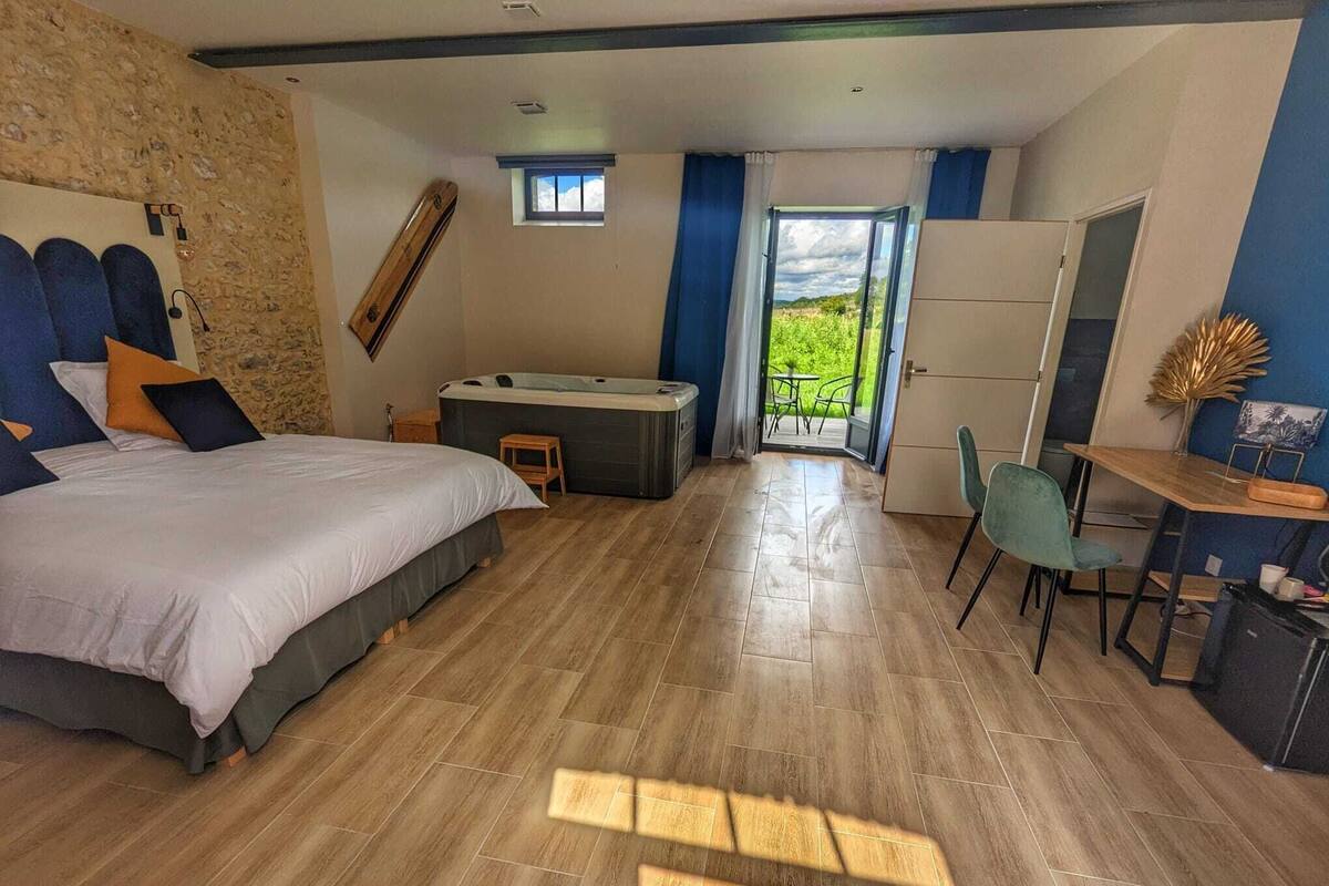 Quarto com cama grande, mesinha, cadeira e banheira de hidromassagem.