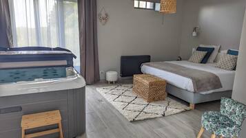 A modern bedroom with a bed, a small sofa, a chair, a hot tub, and a window with curtains.