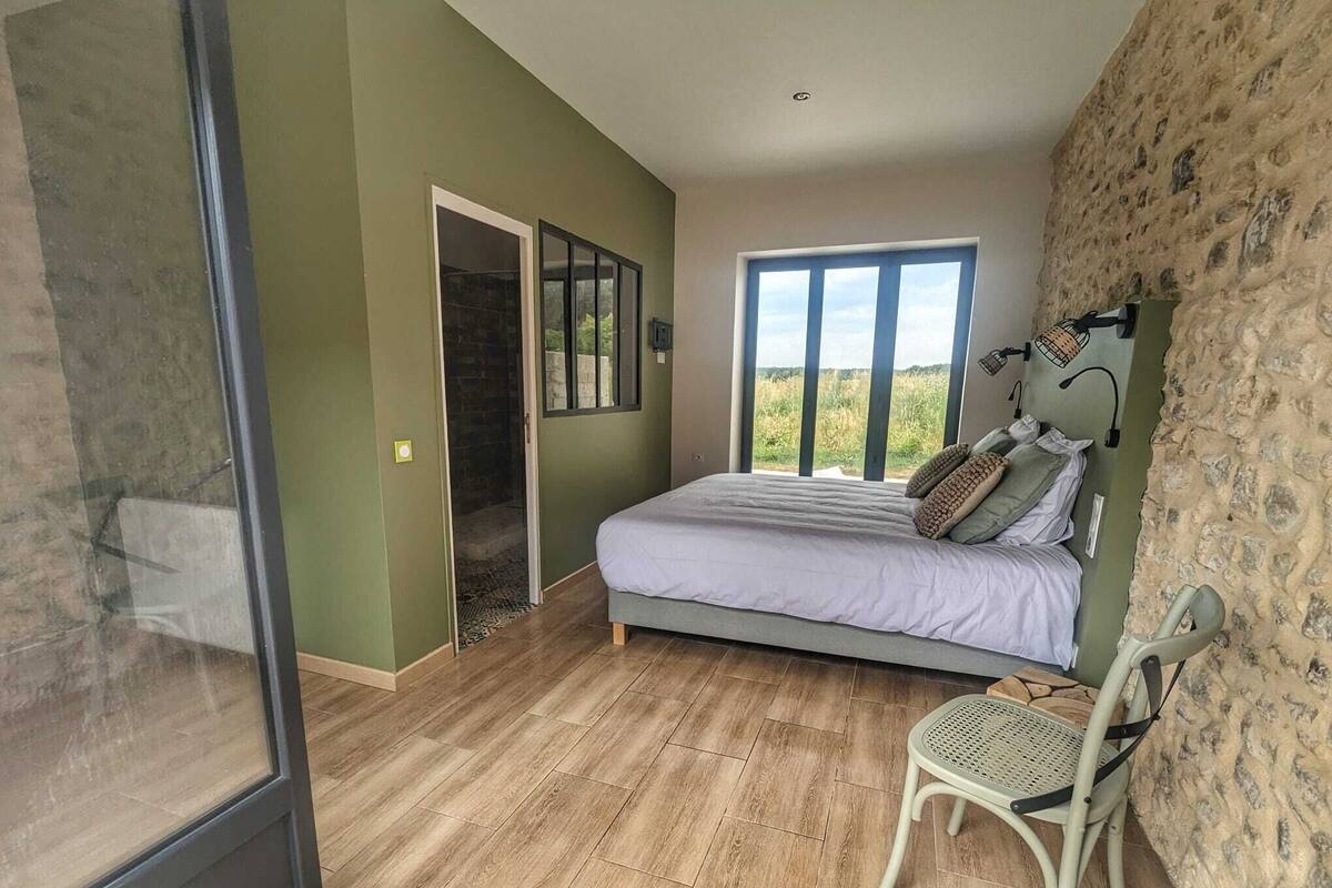 Quarto com cama, cadeira, janela e porta que dá para uma varanda.