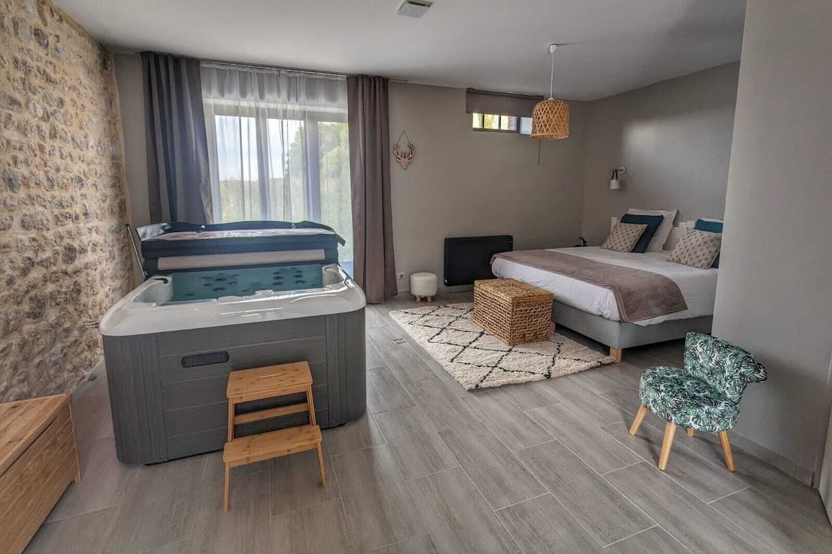 Quarto moderno com uma cama grande, um espaço de estar pequeno, uma banheira de hidromassagem e uma parede de pedra.