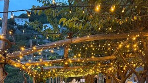 A rustic outdoor seating area with a stone pathway, wooden pergola, and string lights. - Alma Domus ancient house recently opened in Amalfi (Amalfi)