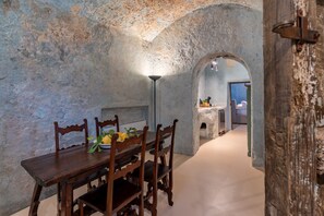Ein rustikaler Essbereich mit Holztisch und -stühlen, einer Lampe und Blick in einen angrenzenden Raum durch einen Bogen.