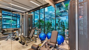A gym with exercise equipment, large windows, and a view of a building with greenery. - B507 - 1 Bedroom Condo Top Floor Pool View, Ao Nang (Krabi)
