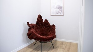 Une pièce avec un fauteuil en velours rouge, un tableau encadré au mur et un plancher en bois.