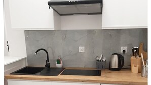 A modern kitchen with a black sink, white cabinets, a marble backsplash, and a compact dishwasher.