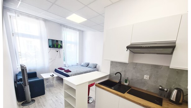 A compact, modern room with a bed, a small table, a TV, and a kitchenette.