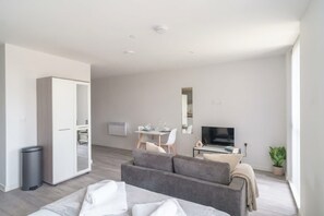 A modern living room with a sofa, a TV, and a dining area with a table and chairs.