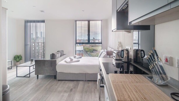 A modern hotel room with a bed, a small seating area, a kitchenette, and a large window offering a city view. - Fabulous Studio in Central Liverpool (Liverpool)