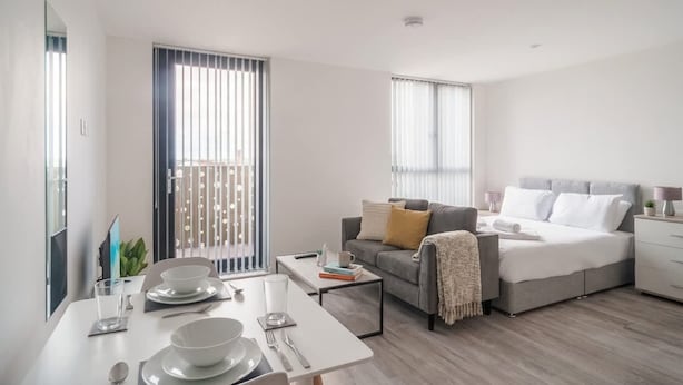 A modern, well-lit living room with a dining area, a sofa, and a bed.