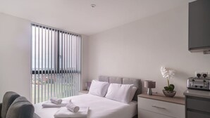 A modern hotel room with a large bed, bedside tables, a TV, and a view through the window blinds. - Fabulous Studio in Central Liverpool (Liverpool)