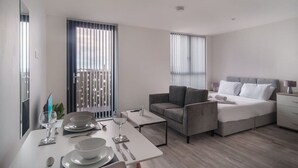A modern, well-lit room with a dining area, a sofa, a bed, and a balcony with a view. - Fabulous Studio in Central Liverpool (Liverpool)