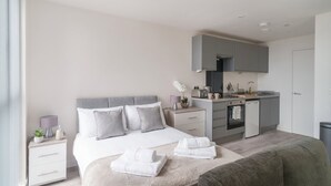 A modern hotel room with a bed, bedside tables, a small kitchenette, and a bathroom.