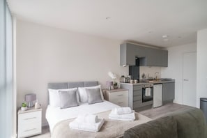 A modern hotel room with a bed, bedside tables, a small kitchenette, and a bathroom.