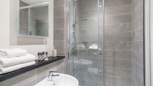A modern bathroom with a glass-enclosed shower, a white sink, and a black countertop with toiletries.