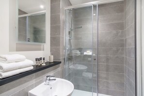 A modern bathroom with a glass-enclosed shower, a white sink, and a black countertop with toiletries.