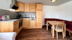 Een compacte keuken met houten kastjes, een inbouwoven, een gootsteen en een eethoek met een houten tafel en stoelen.