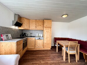 Eine kompakte Küche mit Holzausstattung, einem eingebauten Ofen, einer Spüle und einem Essbereich mit Holztable und Stühlen.