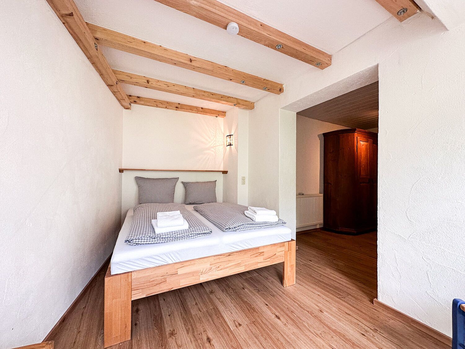 Une chambre à coucher avec un cadre de lit en bois, une literie à carreaux et un plafond en pente avec des poutres apparentes.