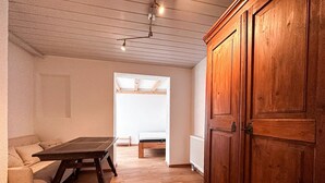 Een kamer met een houten vloer, een bank, een tafel en een kledingkast.