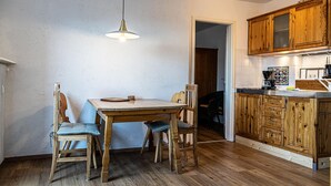 Ein Essbereich mit Holztisch und -stühlen, einer Pendelleuchte und Holzschränken in der angrenzenden Küche.