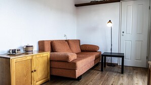Ein kompakter Wohnbereich mit einer Couch, einem kleinen Tisch, einem Schrank und einer Stehlampe.