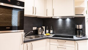 Een moderne keuken met witte kastjes, een zwart aanrecht, een Siemens oven, een koffiezetapparaat en een waterkoker.