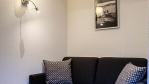 Een donkere bank met gekleurde kussens, een klein glazen tafeltje en een wandlamp.