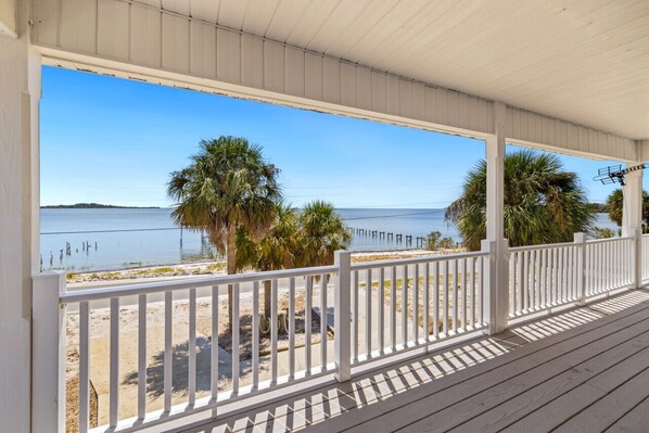 A covered porch with a view of a beach and water.