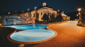 A swimming pool with a curved design, a paved walkway, and a building in the background.