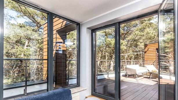 A modern room with large windows, a blue sofa, and a view of an outdoor deck with furniture.