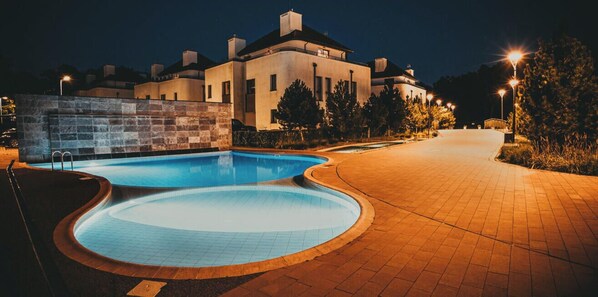 A swimming pool with a curved design, a paved walkway, and a building in the background. - Forest | Plaża | Taras | 2 Poziomy | Blisko Morza (Rogowo)