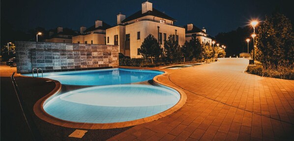 Une piscine au design incurvé, un chemin pavé et un bâtiment en arrière-plan.