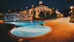 Una piscina de diseño curvo, un sendero empedrado y un edificio al fondo.