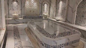 A luxurious bathroom with a large marble bathtub, intricate tile patterns, and arched windows with decorative glass. - Malnad Shire (Shimoga)