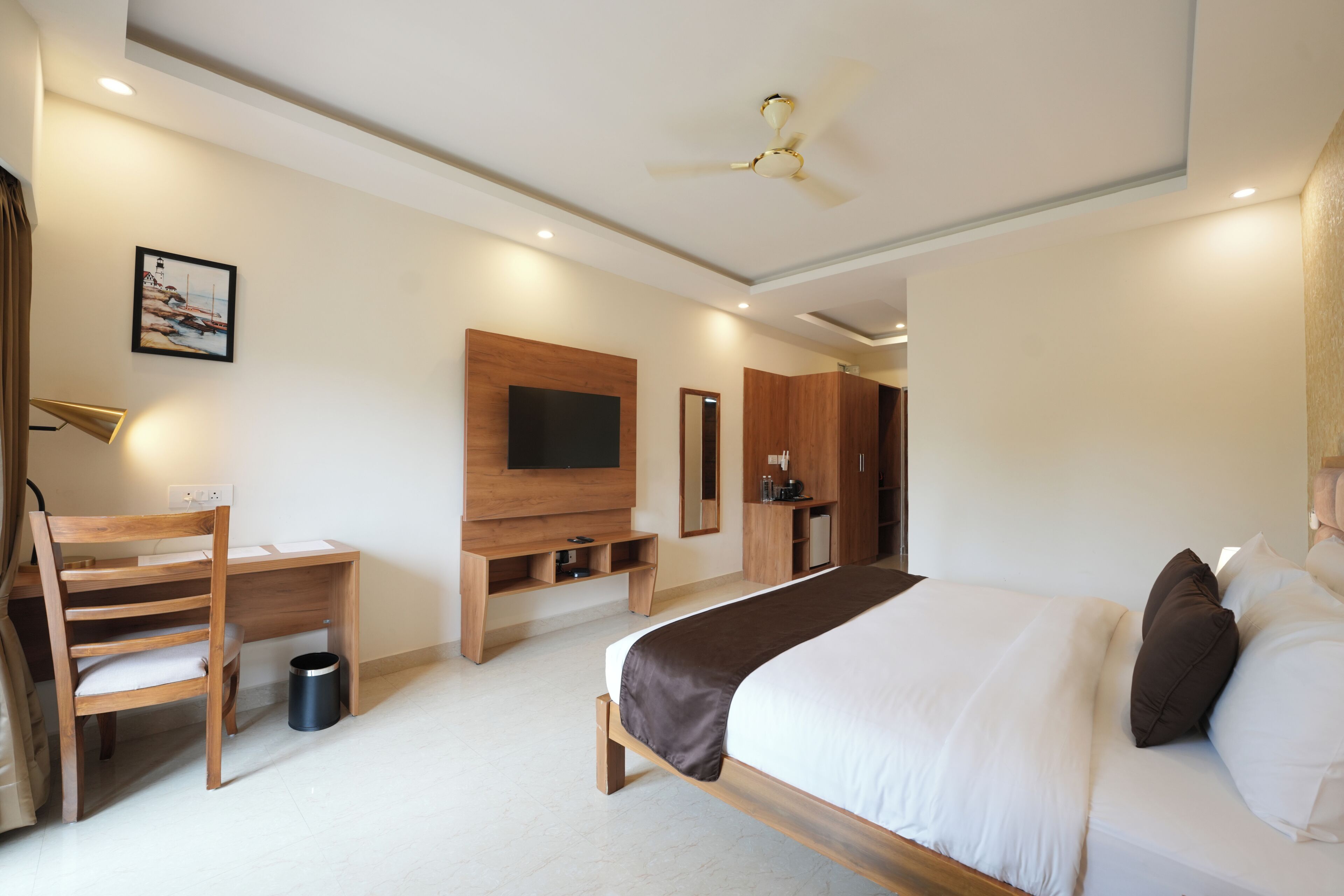 A modern hotel room with a bed, desk, chair, TV, and a ceiling fan.