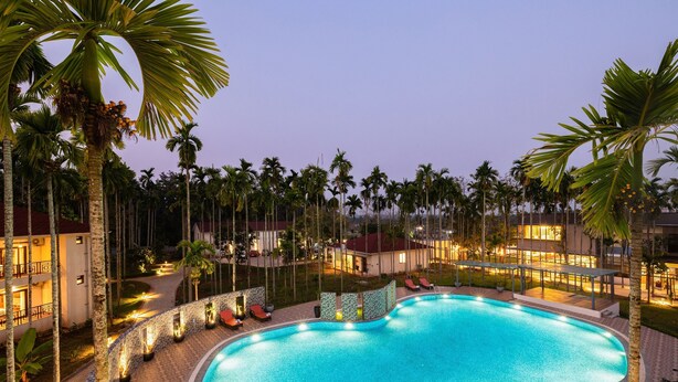 A swimming pool surrounded by palm trees and a building with a red roof. - Malnad Shire (Shimoga)