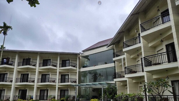 Un hotel de varios pisos con balcones, un atrio central de vidrio y un patio con vegetación.