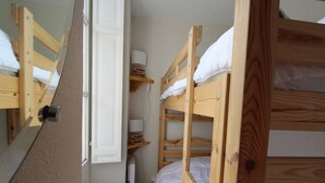 Ein Schlafsaalzimmer mit Stockbetten, einem kleinen Regal mit einer Lampe und einer Tür zu einem weiteren Zimmer.