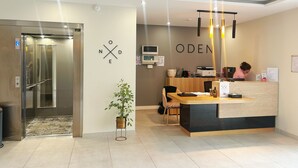 Un área de recepción con mostrador, una planta, un microondas y un letrero con la palabra 'ODEN'.