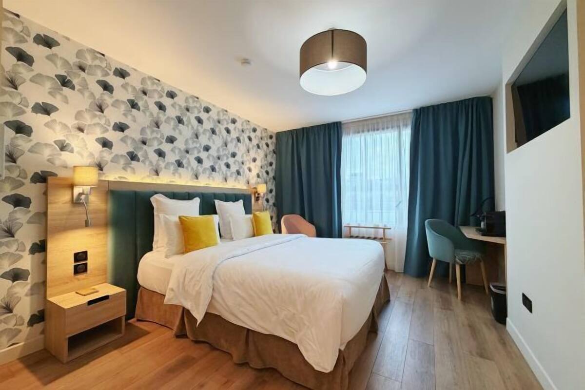 Ein Hotelzimmer mit Bett, Schreibtisch, Stuhl, Nachttisch und einer Wand mit Blättermotiv.