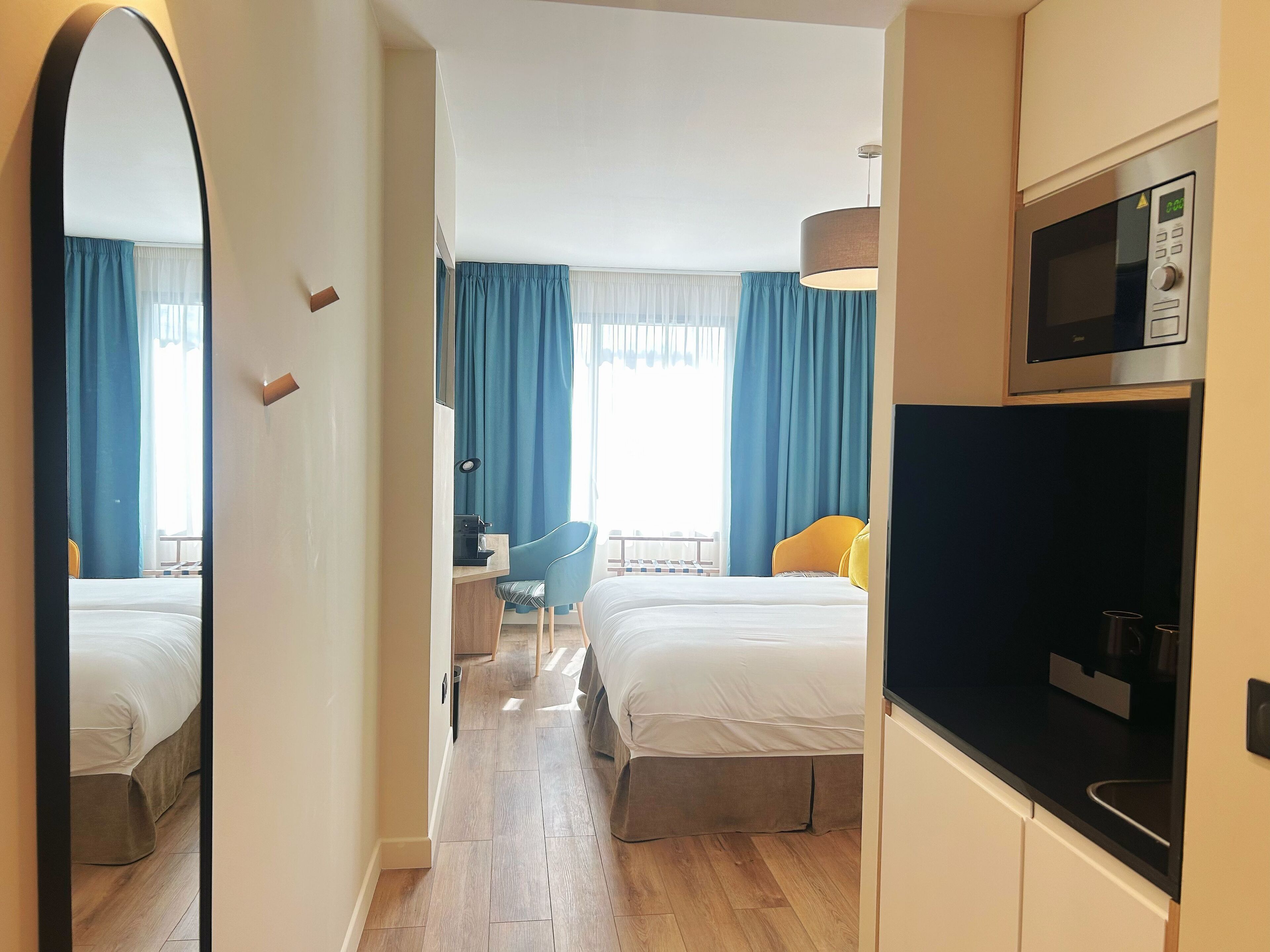 Une chambre d’hôtel avec deux lits, un bureau avec une chaise, un four à micro-ondes et un grand miroir.