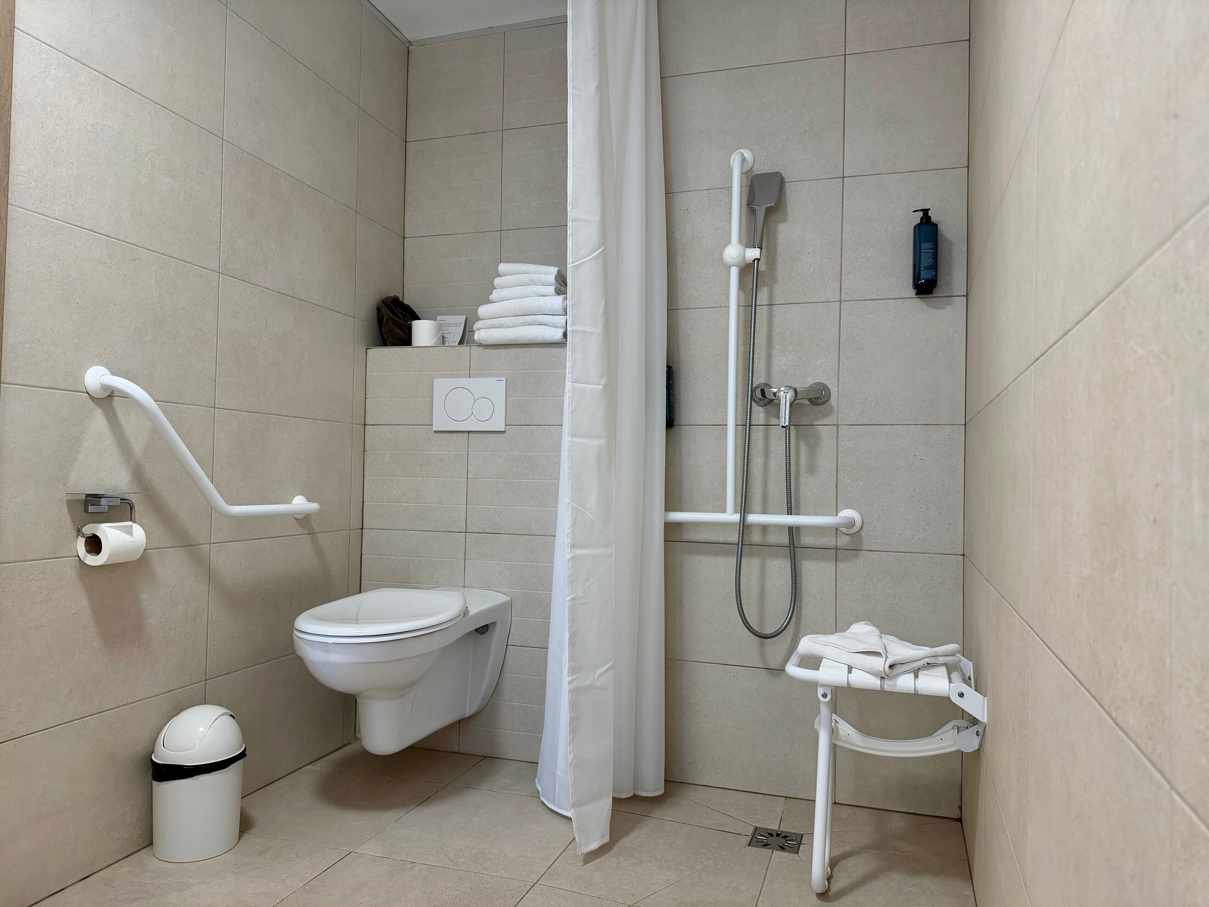 Un baño moderno con inodoro, ducha y barras de apoyo.
