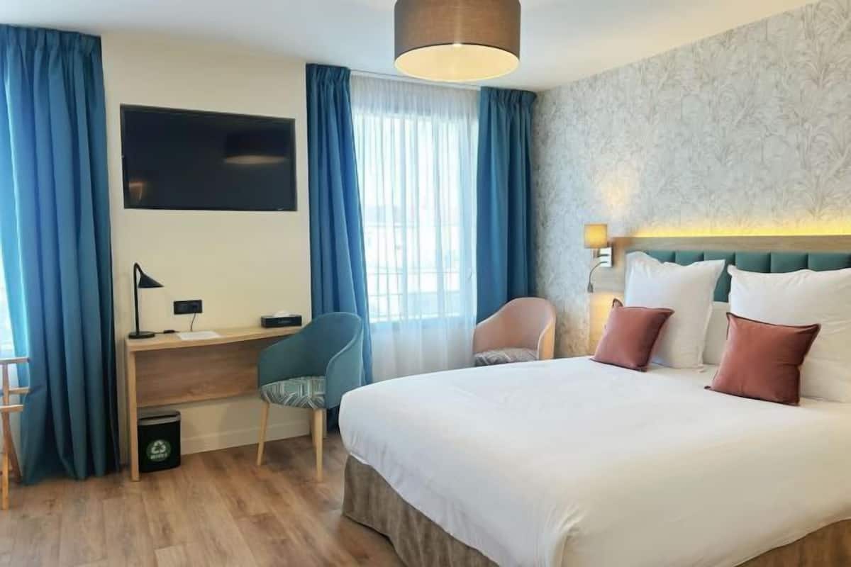Ein Hotelzimmer mit Bett, Schreibtisch, Stuhl und Fernseher an der Wand.